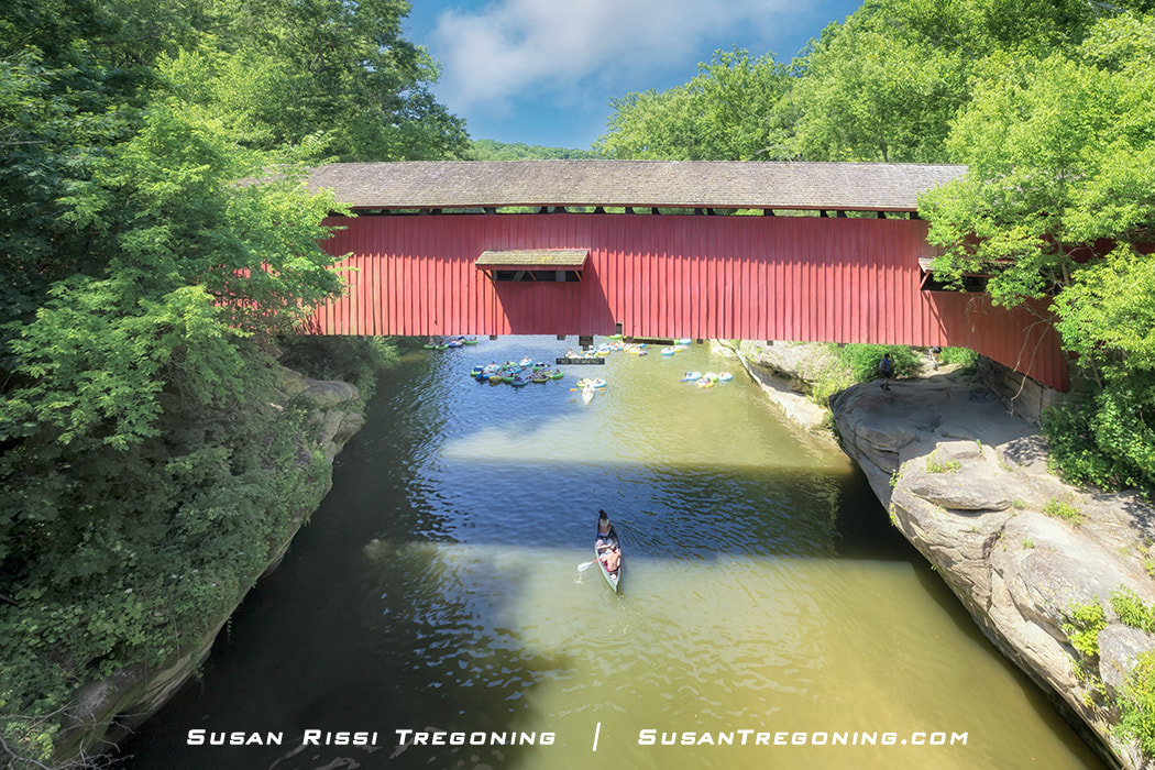 People enjoy the warm summertime weather, floating down Sugar Creek and under the Narrows Covered Bridge in inner tubes and canoes. The Narrows Covered Birdge is part of Turkey Run State Park in Parke County, Indiana.