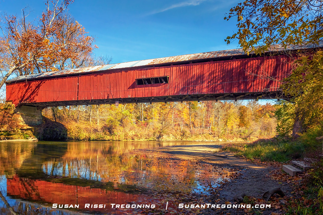 Fall colors reflect on Sugar Creek under the Cox Ford Covered Bridge in Parke County, Indiana.