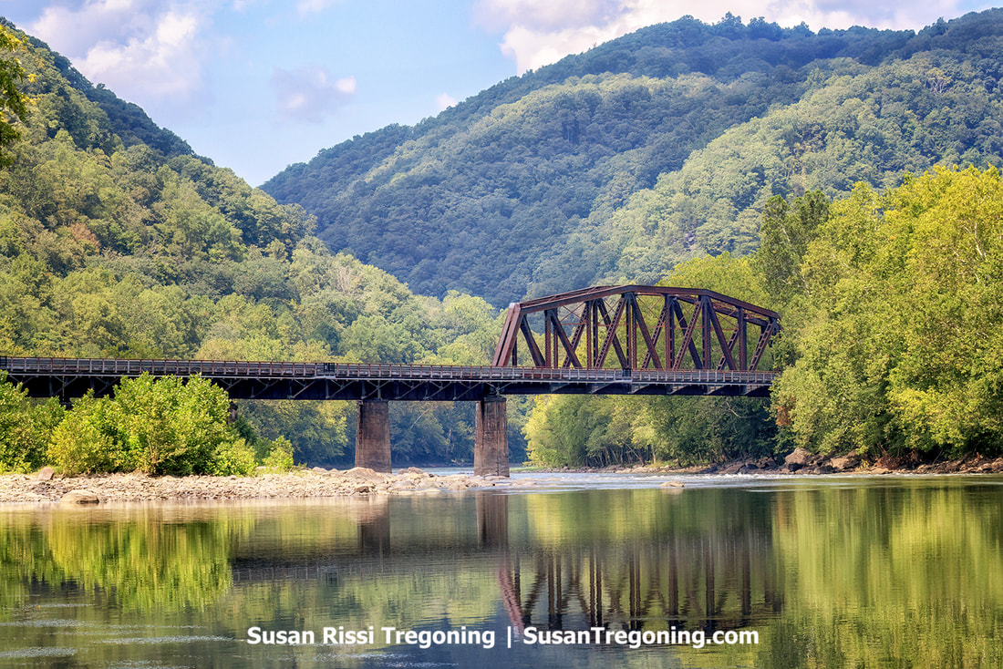 At the bridge crossing to the ghost town of Thurmond, West Virginia, the water of the New River mirrors the historic Thurmond Railroad Bridge in a picturesque display at the New River Gorge National Park.