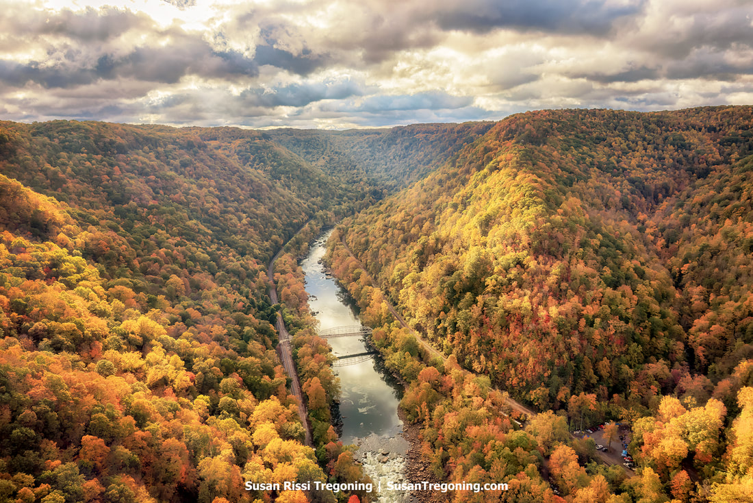 From atop the 876-foot-high New River Gorge Bridge, one can see an awe-inspiring vista of the New River Gorge during Autumn. This sight is exclusive to Bridge Day, the one day of the year when traffic halts for BASE jumping events, and individuals can stroll across it.